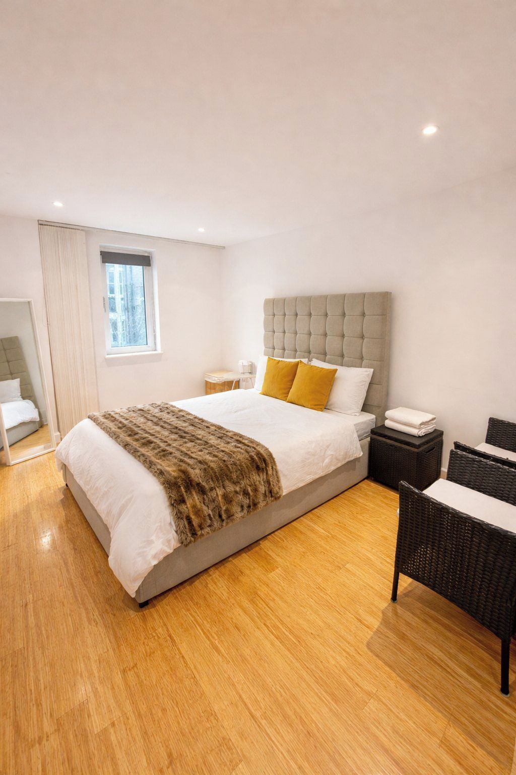 Una habitación de hotel moderna con una cama grande, una mesita de noche, una silla y un ventanal.