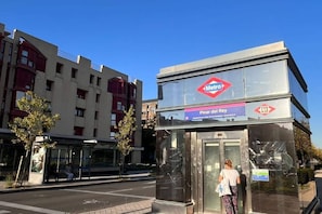 A Metro station with a clear sky, a bus stop shelter, and a building with a red and white facade. - Stay in Quiet Madrid Area (Madrid)