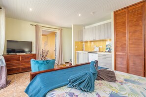 Ein Hotelzimmer mit einem Bett, einem Fernseher, einer Holzkommode, einem Essbereich mit Tisch und Stühlen sowie einer Küchenzeile.