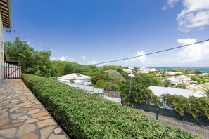 A residential area with a stone pathway, lush greenery, and houses with white roofs. - Le Cocon de la Villa Soleil - Studio avec Vue Mer (Le Robert)