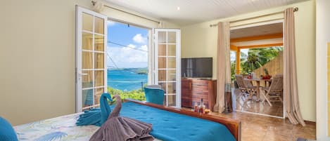 Un dormitorio con una cama grande, vista al mar y una puerta abierta que da a un comedor.
