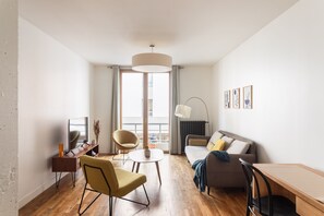 A modern living room with a sofa, armchair, dining table, and a TV. - L'Archi - Maison de ville pour 6 (Rennes)