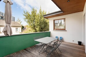 A balcony with a table and chairs, a window, and a view of trees and buildings. - L'Archi - Maison de ville pour 6 (Rennes)