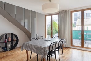 A dining area with a table set for four, a staircase, and a view of a pool through a glass door. - L'Archi - Maison de ville pour 6 (Rennes)