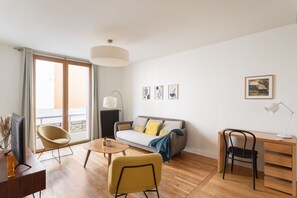 Een moderne woonkamer met een bank, stoelen, een bureau en een groot raam.