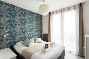 A hotel room with a bed, a nightstand, a wall-mounted lamp, a radiator, and a window with curtains. - L'Archi - Maison de ville pour 6 (Rennes)