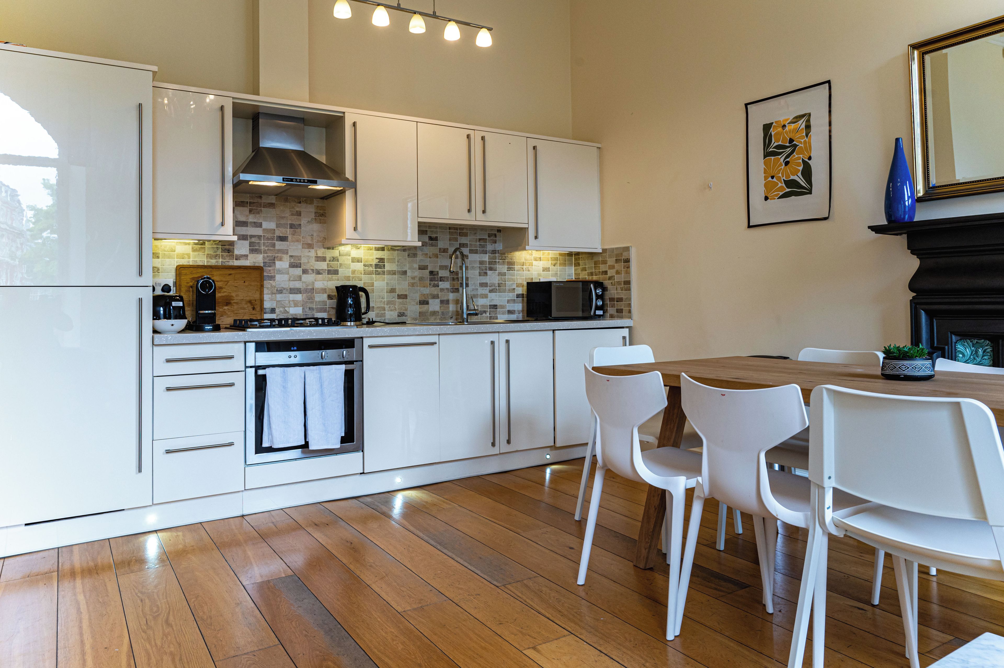 Een moderne keuken met witte kastjes, een houten eettafel en stoelen.