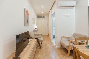 Un salon moderne comprenant un téléviseur à écran plat, un canapé, une table basse en bois et une table à manger avec des chaises.