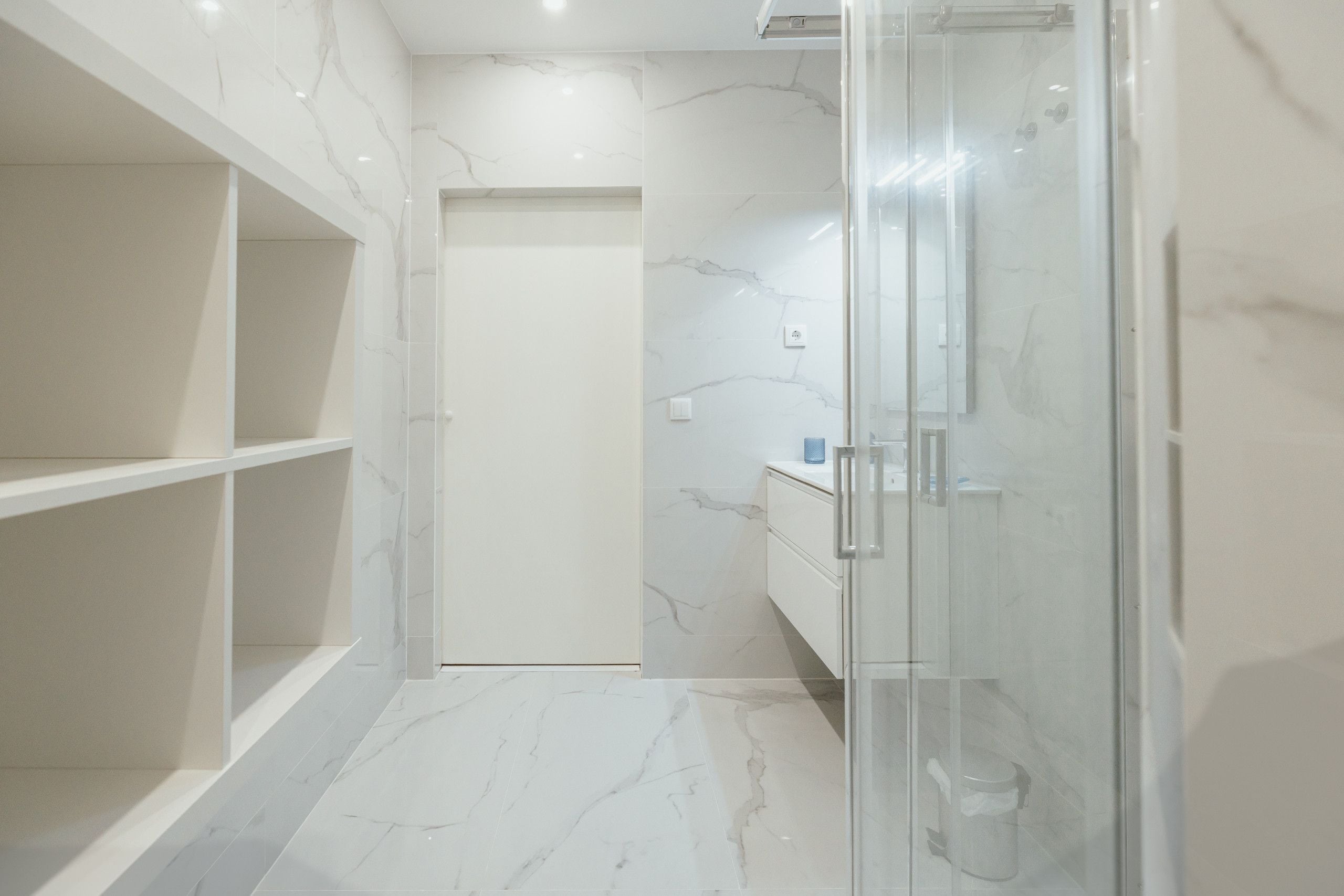 Een moderne badkamer met een douchecabine van glas, marmeren vloeren en inbouwkasten.
