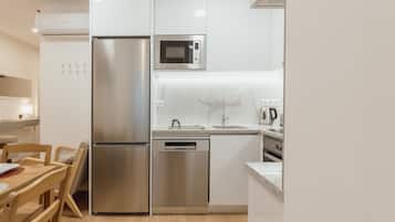 A compact kitchen with a stainless steel refrigerator, a microwave, a dishwasher, and a sink with a marble countertop.