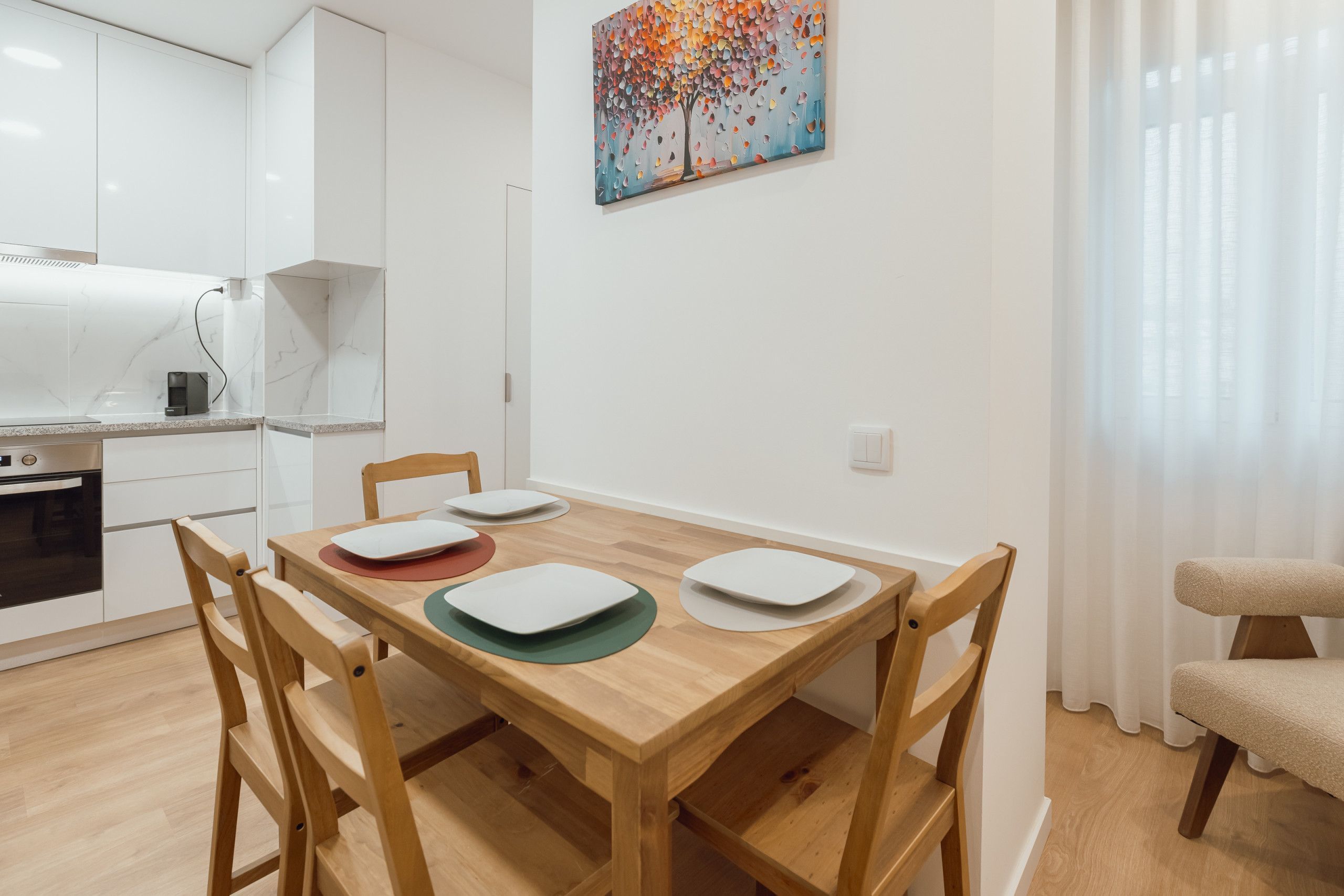 A modern kitchen with white cabinets, a built-in oven, and a dining area with a wooden table and chairs.