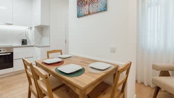 A modern kitchen with white cabinets, a built-in oven, and a dining area with a wooden table and chairs.