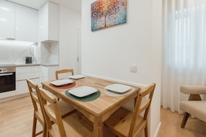 Une cuisine moderne avec des armoires blanches, un four encastré et un coin repas comprenant une table et des chaises en bois.