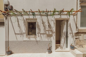A building facade with a textured wall, a wooden pergola with climbing plants, a window, and a door. - Typical JOY Duplex by Vacationy (Porto)