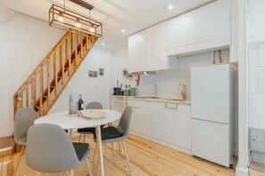 A modern kitchen with white cabinets, a wooden staircase, and a dining area with two chairs and a table. - Typical JOY Duplex by Vacationy (Porto)