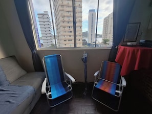 Una habitación con sofá, dos sillas, una mesa con mantel rojo y ventana con vista a edificios.