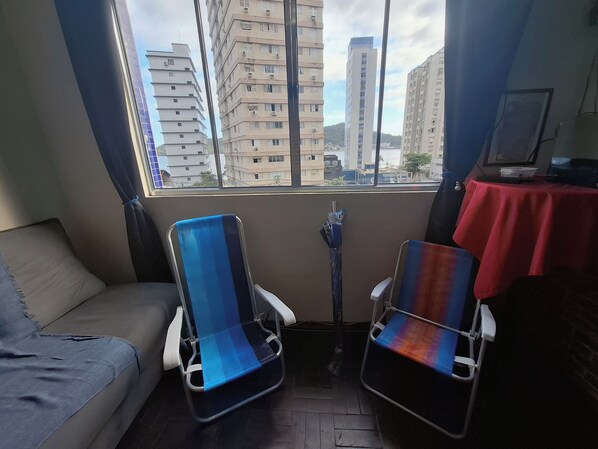 A room with a sofa, two chairs, a table with a red tablecloth, and a window with a view of buildings.