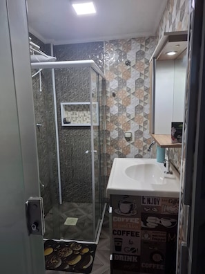 Un baño con ducha envuelta en vidrio, un lavabo blanco y un salpicadero de azulejos.