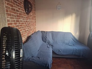A room with a brick wall, a bed with a blue blanket, a black fan, and a wall-mounted sign.
