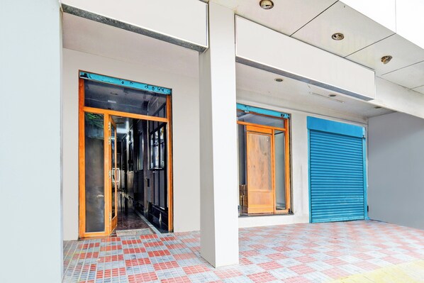 A building entrance with a tiled floor and two doors, one with a blue shutter and another with a wooden frame.