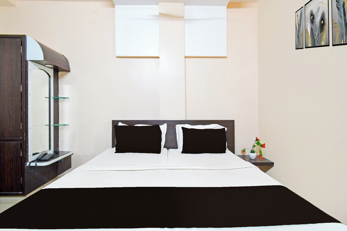 A hotel room with a bed, a desk with a telephone, a mirror, and a small table with a vase of flowers.