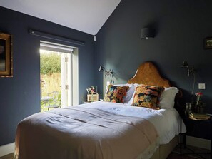 Ein Schlafzimmer mit einem großen Bett, einem Nachttisch, einer Lampe und Blick ins Freie.