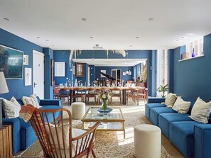 A spacious living room with a dining area, featuring blue walls, a piano, and a large window. - The Renard - 19-23 Guests (Payhembury)