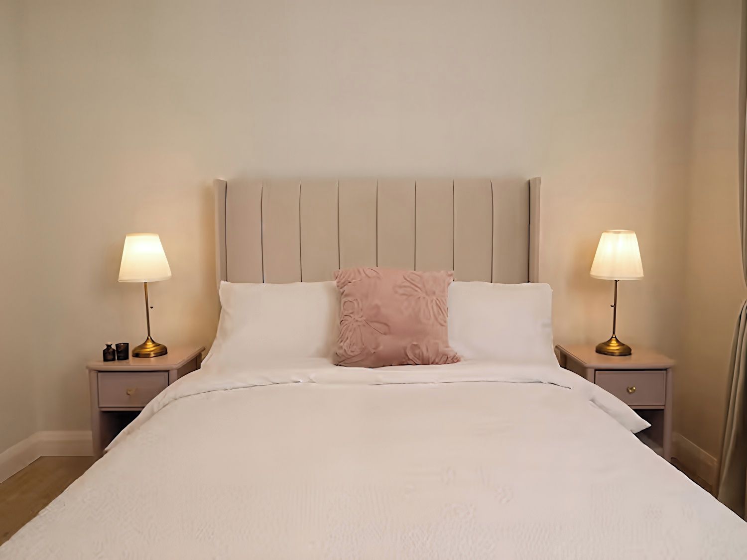 A neatly made bed with a headboard, two bedside tables with lamps, and a decorative pillow.