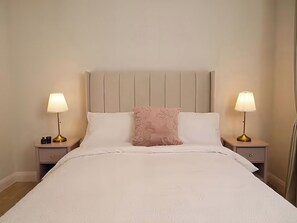 A neatly made bed with a headboard, two bedside tables with lamps, and a decorative pillow. - Long Meadow Apartment (Ballymena)