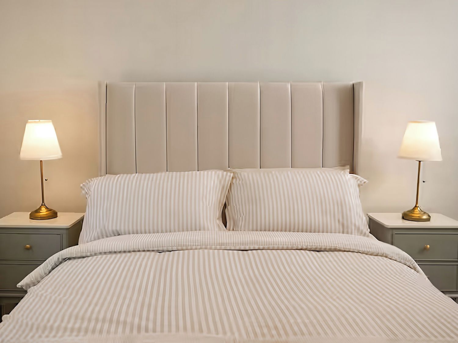 A bed with a striped bedspread, two bedside tables with lamps, and a padded headboard.