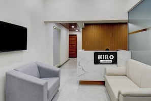 A hotel reception area with a marble reception desk, a grey armchair, and a white sofa.
