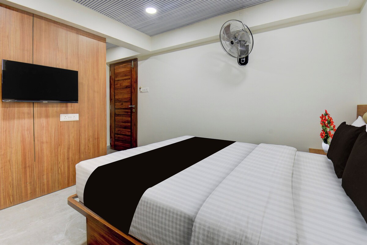 A hotel room with a bed, a television mounted on the wall, a ceiling fan, and a wooden wardrobe.