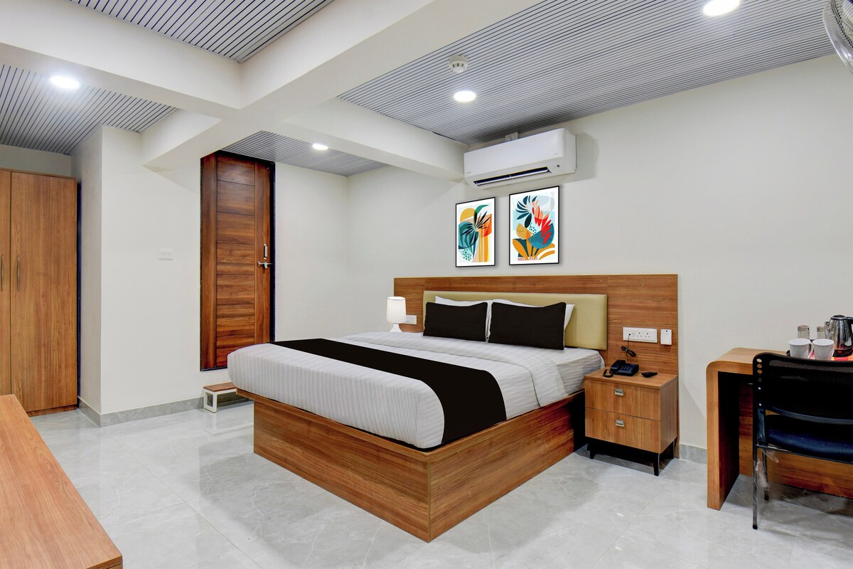 A modern hotel room with a wooden bed, bedside table, and a desk with a chair.