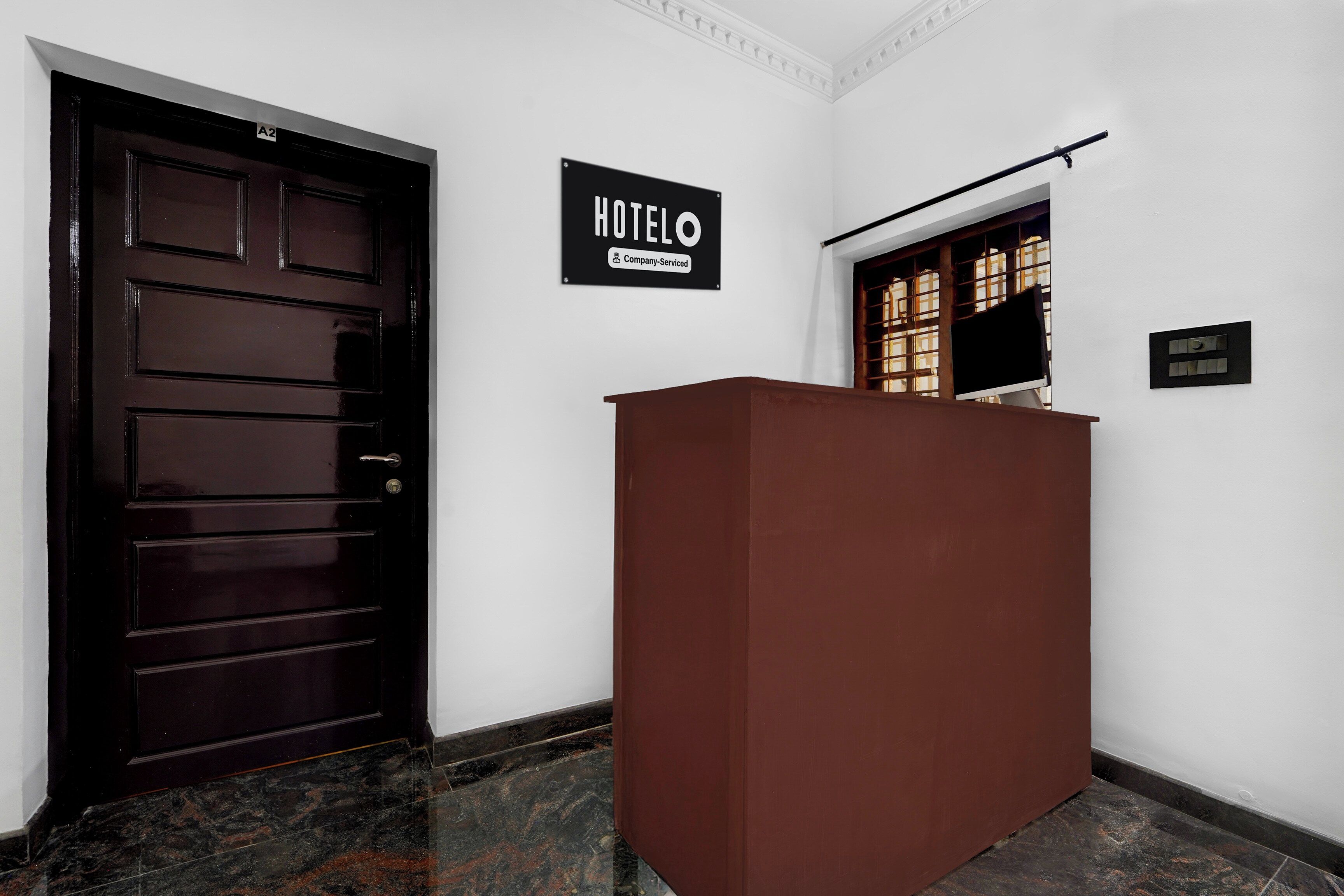 A hotel reception area with a dark wooden door, a reception desk, and a sign indicating the hotel name.