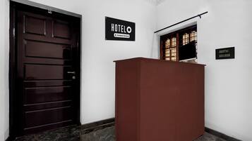 A hotel reception area with a dark wooden door, a reception desk, and a sign indicating the hotel name.