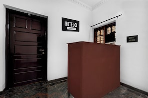 Zona de recepción de un hotel con una puerta de madera oscura, un mostrador de recepción y un cartel con el nombre del hotel.