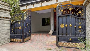 A gated entrance with decorative metalwork and a paved pathway leading to a building with a yellow facade and a window.