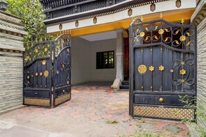 Una entrada con puerta y detalles decorativos de metal, un camino pavimentado que lleva a un edificio con fachada amarilla y una ventana.