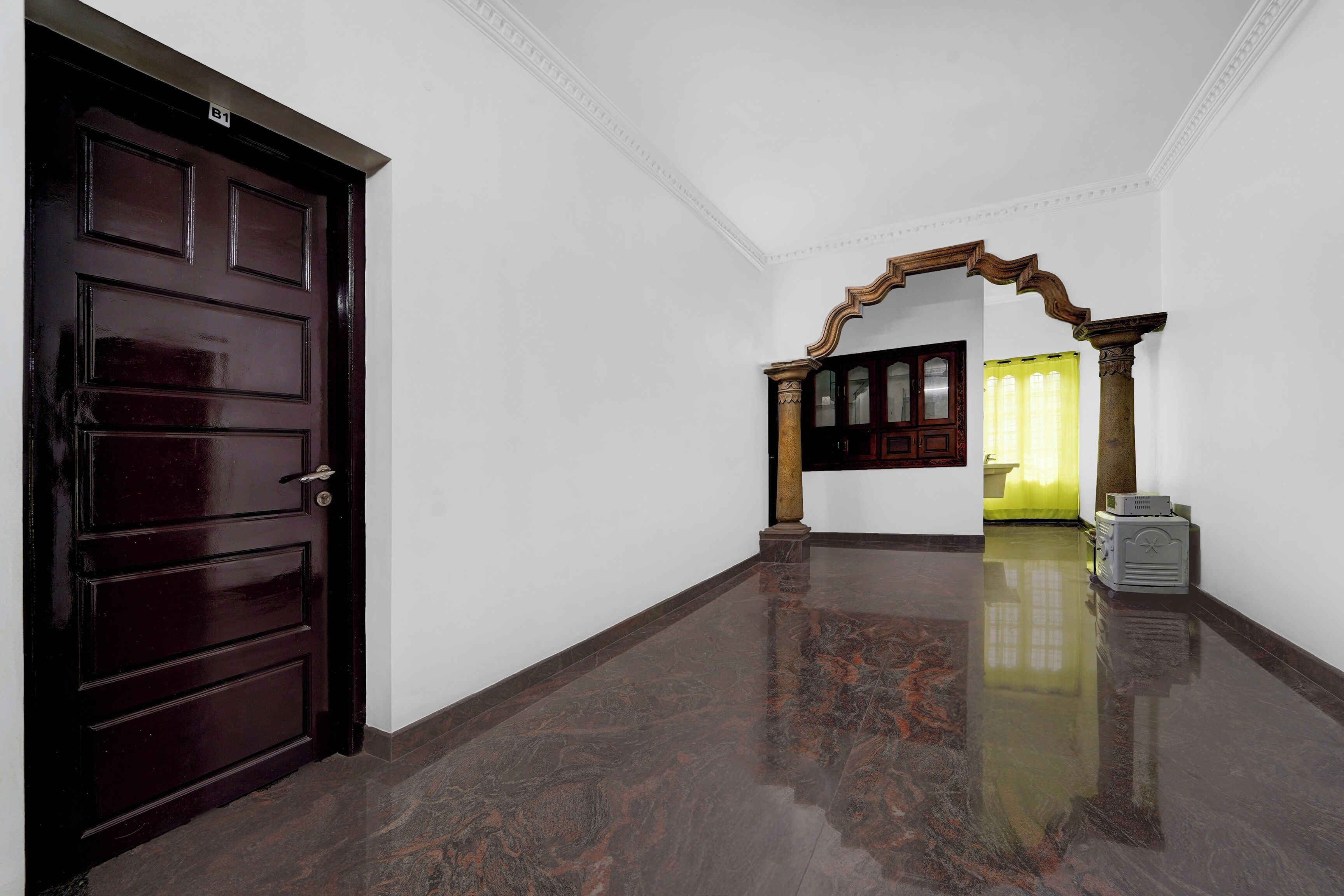 A hallway with a dark wooden door, a marble floor, and a wooden archway leading to a room with a yellow curtain.