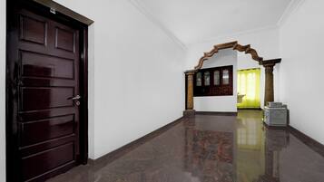 A hallway with a dark wooden door, a marble floor, and a wooden archway leading to a room with a yellow curtain.