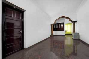 Un pasillo con una puerta de madera oscura, suelo de mármol y un arco de madera que conduce a una habitación con cortina amarilla.