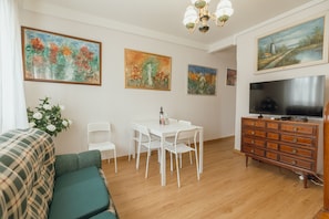 A living room with a sofa, a dining table with chairs, a TV on a wooden cabinet, and paintings on the wall. - Lusa Gaia S House by Vacationy (Vila Nova de Gaia)