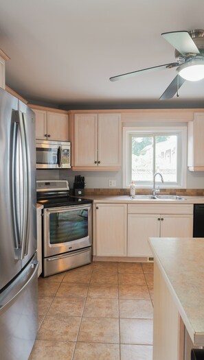 A modern kitchen with stainless steel appliances, a window, and a ceiling fan. - The Beach House - Deeded Beach Access (Brights Grove)