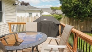 Une terrasse avec une table en verre, deux chaises et un barbecue.