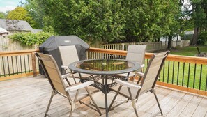 Une terrasse extérieure avec une table ronde et quatre chaises, entourée d’une clôture en bois et d’arbres.