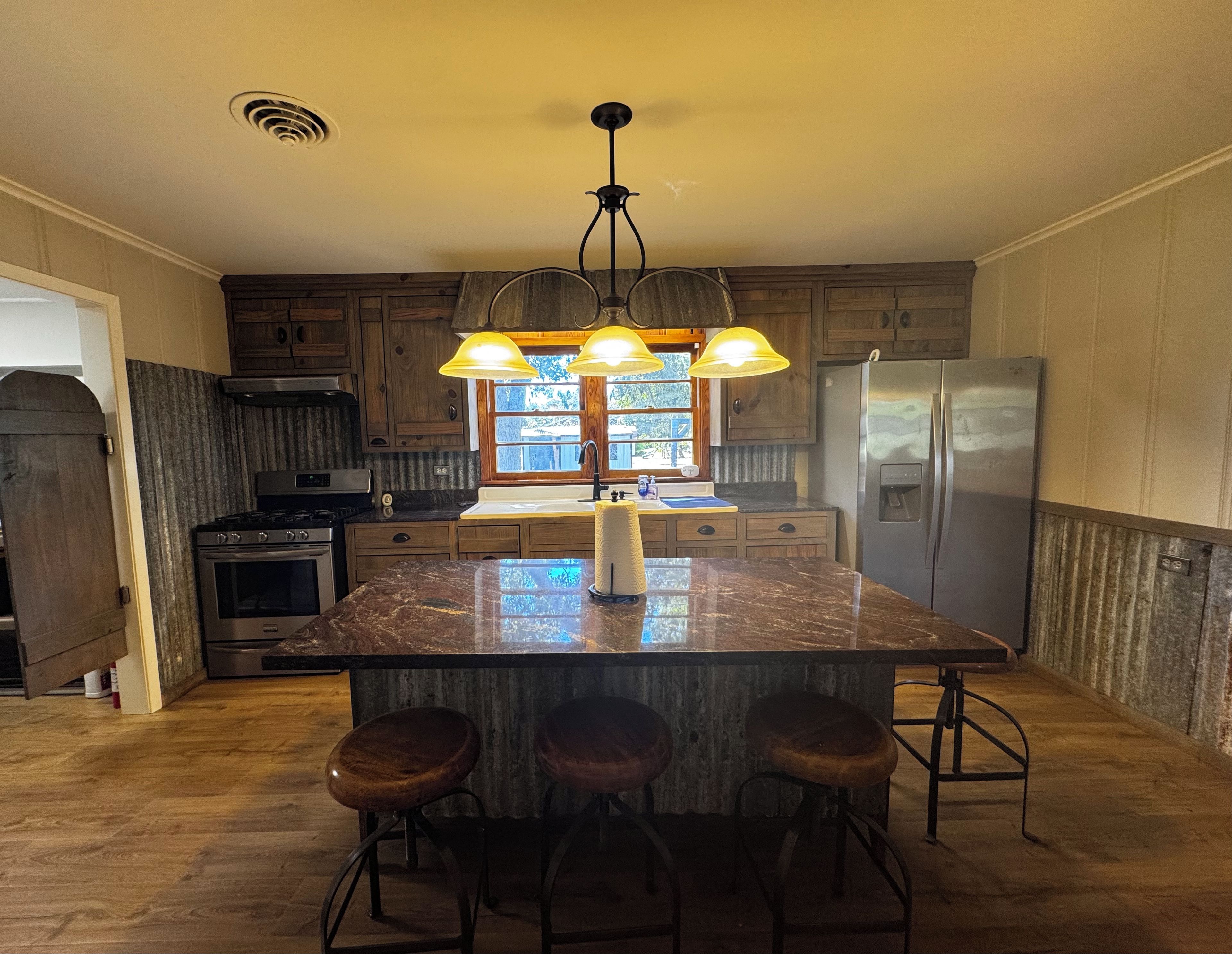 A kitchen with a central island, bar stools, a refrigerator, and wooden cabinets.