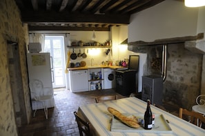 A rustic kitchen with a dining table set for a meal, a wood-burning stove, and various kitchen appliances. - Holiday Home 'Gîte De Thivelle' with Private Garden and Wi-Fi (Cussy-en-Morvan)