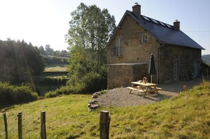 Ein Haus aus Stein mit einem geneigten Dach, einem Holztisch und einer Bank davor.