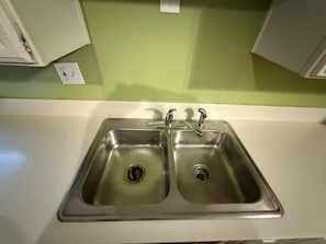 A kitchen with a double stainless steel sink, a white countertop, and a green wall.