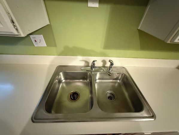 A kitchen with a double stainless steel sink, a white countertop, and a green wall. - Row House Suite 927 (Topeka)